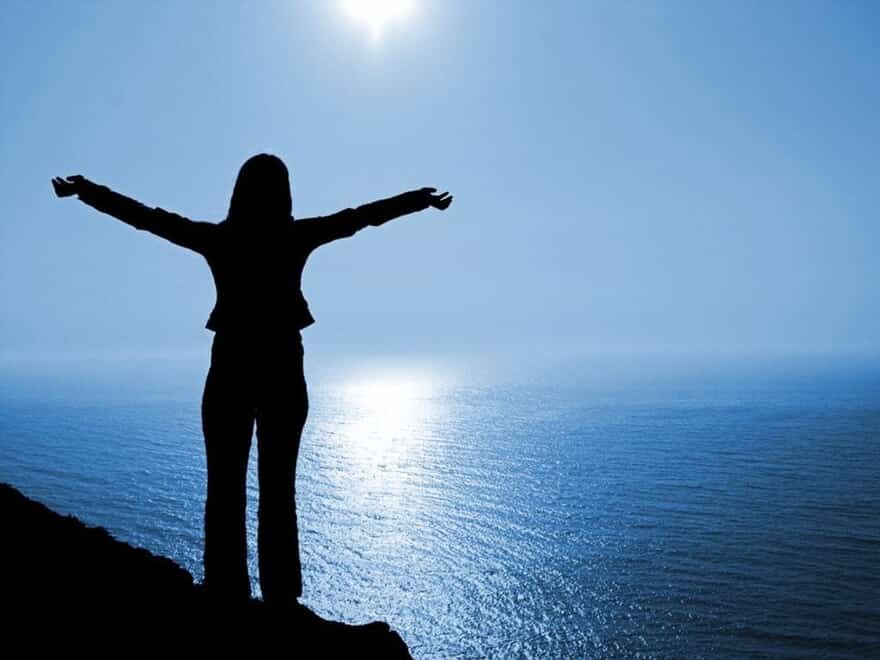 Image of woman with arms wide open on cliff overlooking the ocean