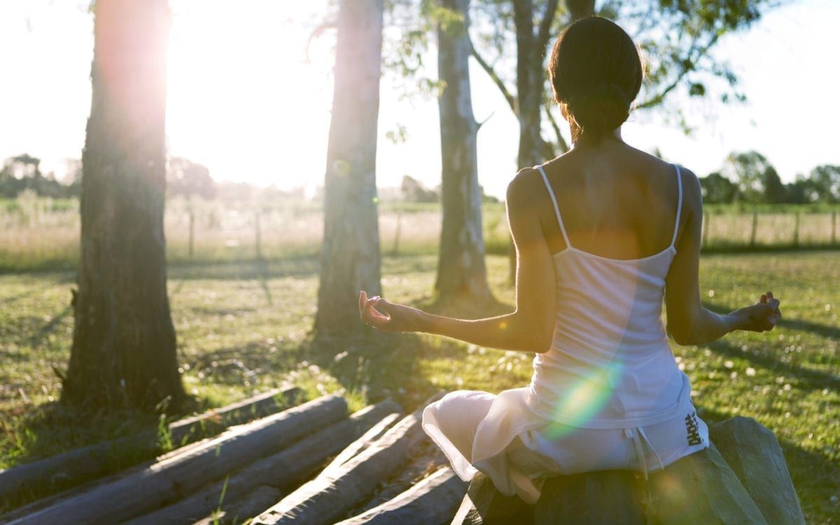 Image of a woman meditating surrounded by trees