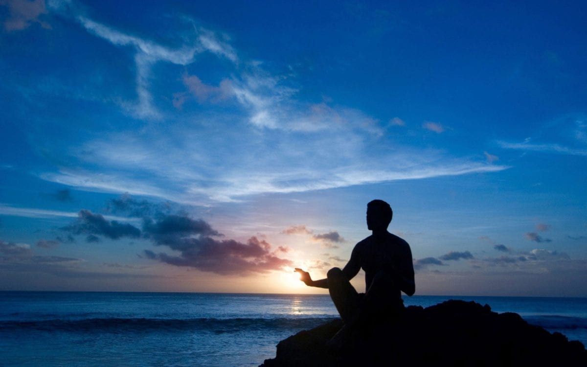Image of a man meditating near the ocean